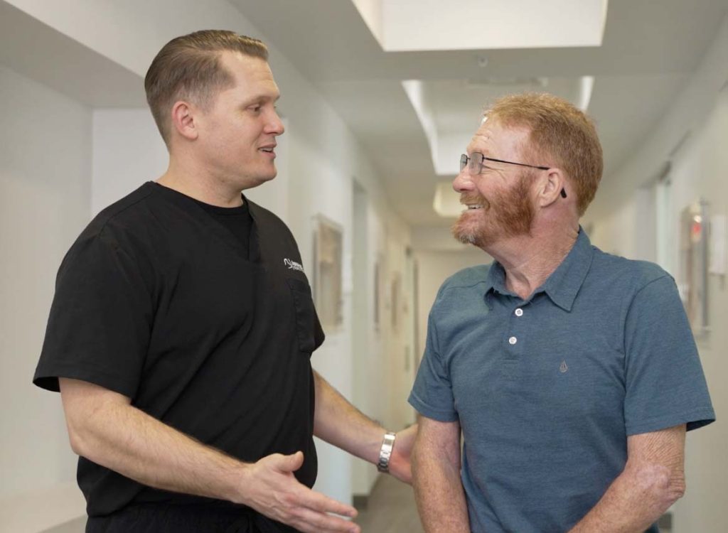 Dentist from Advanced Dental in Lewisville talking with a happy implant patient.