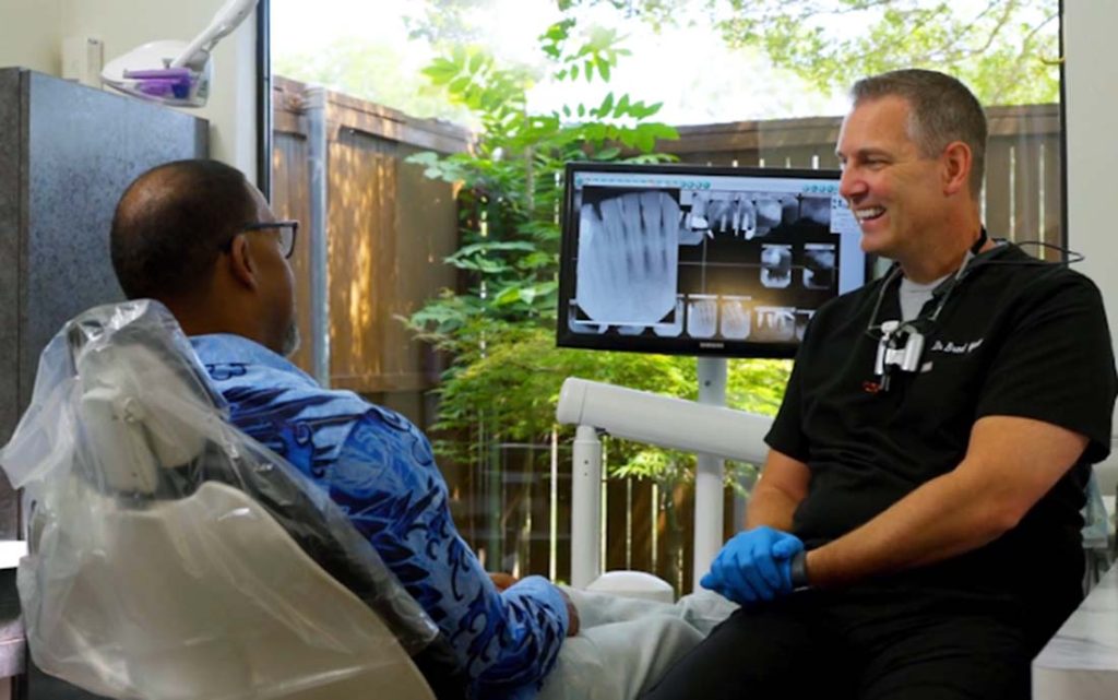 Dentist in scrubs talking with a patient sitting in a dental chair.