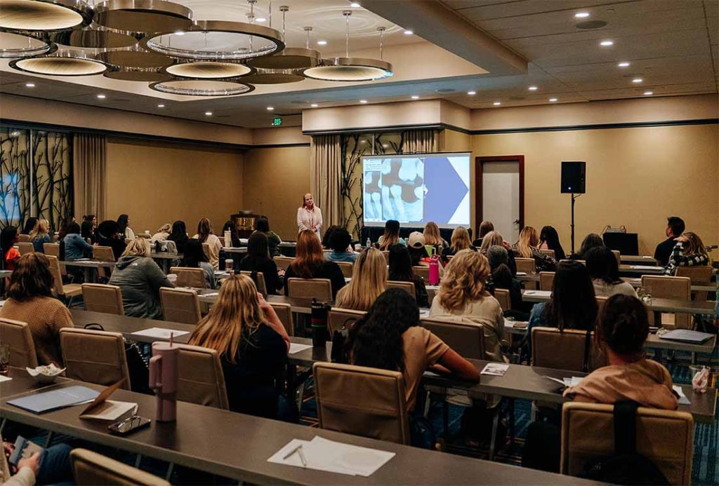 Dentist giving a presentation to a group of dentists and staff at a continuing education event.